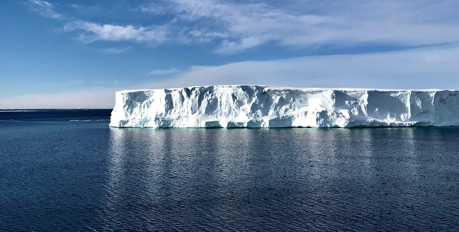 Blue ocean with a white iceberg in the distance and a bright blue sky