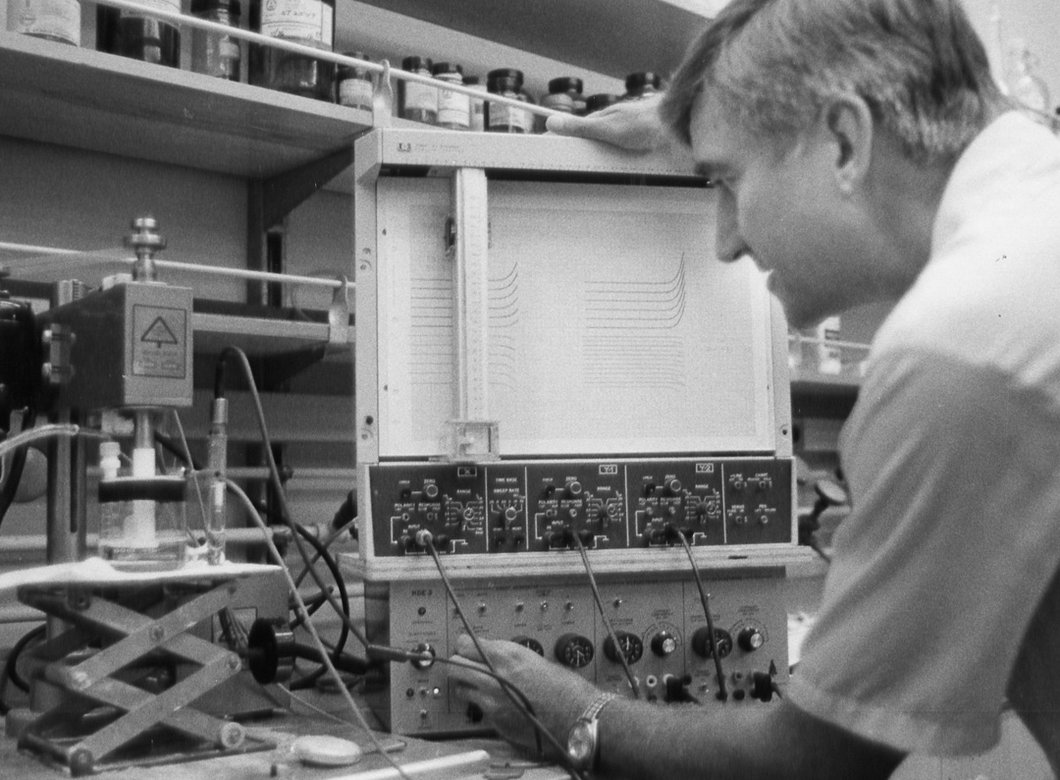 A man seen from behind, adjusting scientific equipment in a chemistry lab.