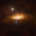 A glowing disc of material with cloudlike material around it are lit up in the center of a dark image with a few bright starlike spots.