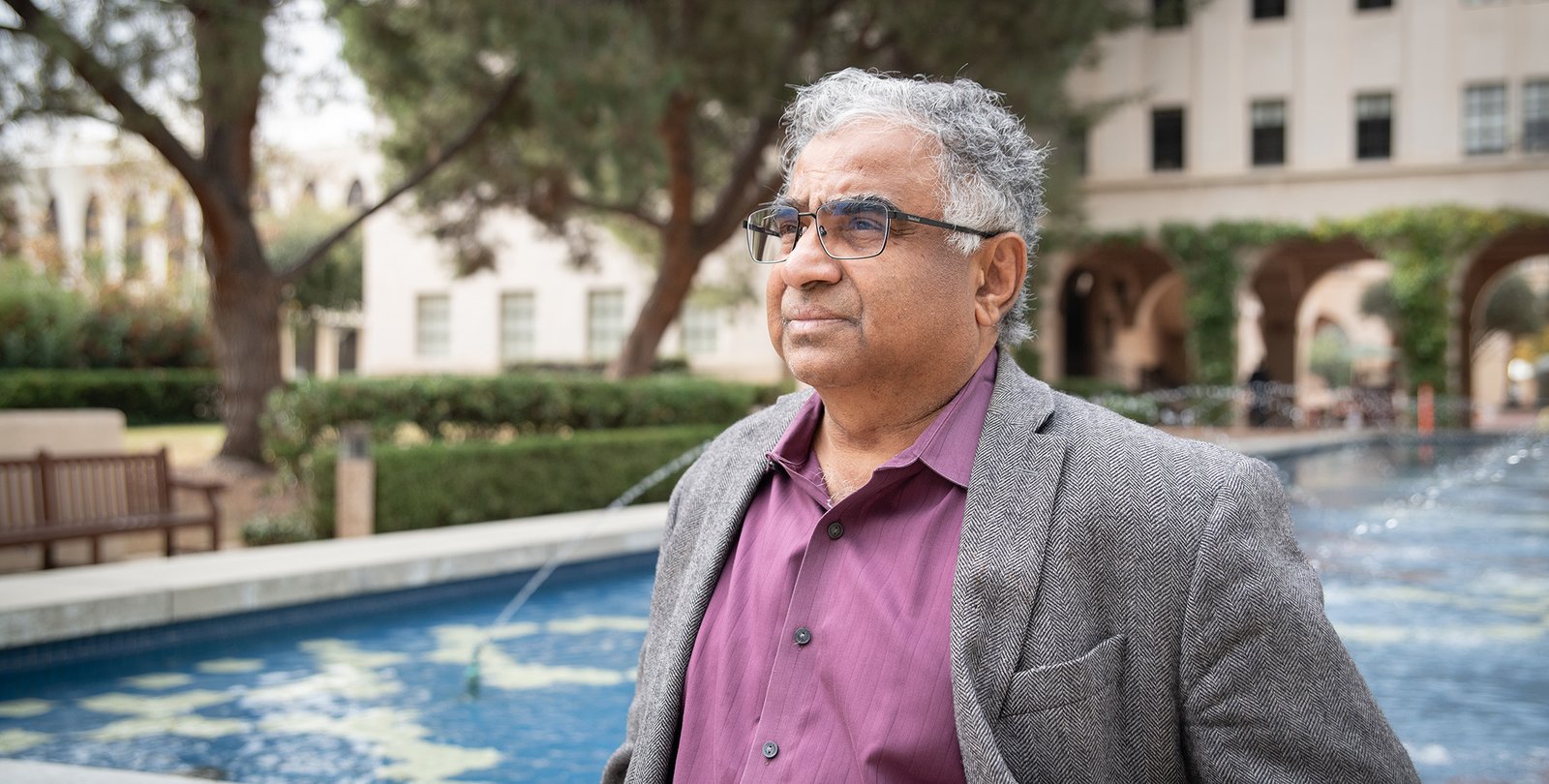 Image of Shri Kulkarni in purple shirt and grey blazer in front of fountain
