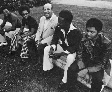 image from 1975 of four students and administrator sitting on a low wall
