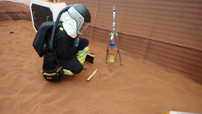 Caltech alumnus Ross Brockwell (MS '01) wears a dark spacesuit as he conducts a mission on the red surface of a Mars simulation.