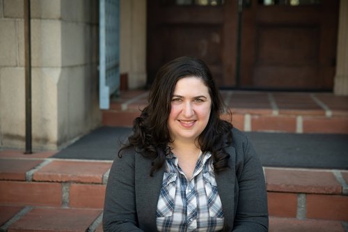 A portrait of Lisa Ruth Rand. She sits upon brick steps in a doorway.