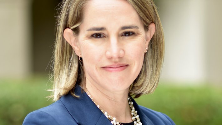 A photo portrait of a woman with blond hair wearing a blue blazer and black shirt with a chunky pearl necklace.