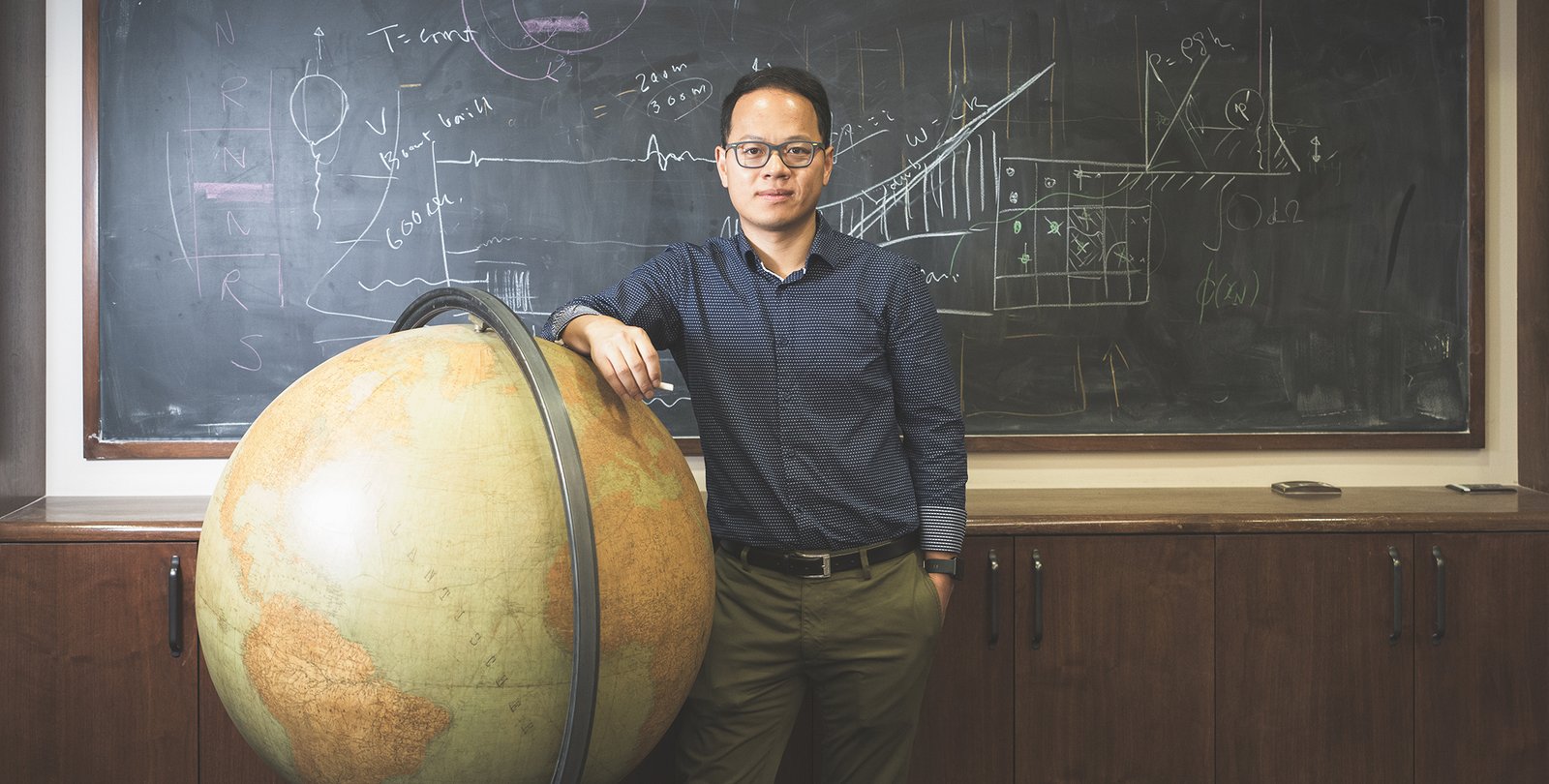 Image of Zhongwen Zhan standing next to a globe in front of a chalk board